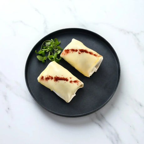 Two uncooked smoky pulled pork pastry parcels on a black plate with fresh greens