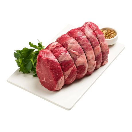 Raw Angus rump roast tied on a white tray with fresh herbs and seasoning bowl