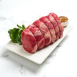 Raw Angus rump roast sliced on a platter with herbs and seasoning on a marble surface