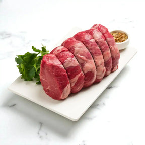 Raw Angus rump roast sliced on a platter with herbs and seasoning on a marble surface