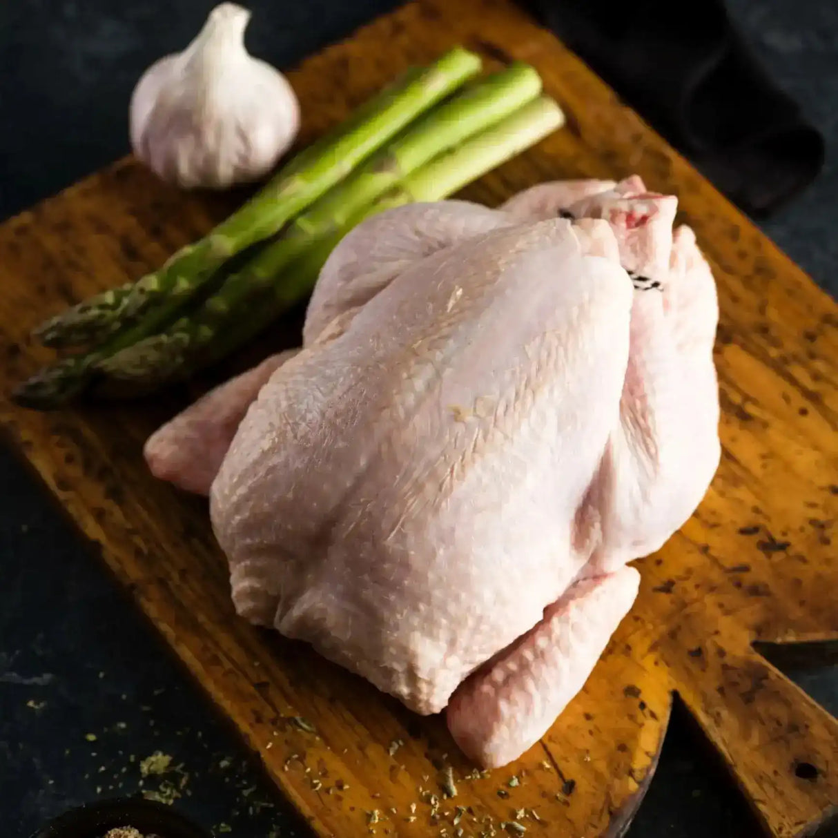 Peter Augustus free range whole chicken on wooden board with asparagus and garlic