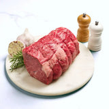 Raw Wagyu rump roast on marble board with garlic, rosemary, salt and pepper shakers