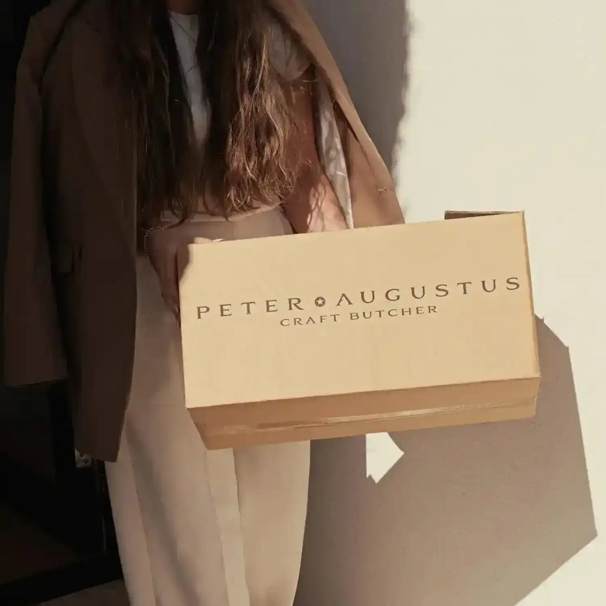Woman holding Peter Augustus Craft Butcher delivery box in natural sunlight