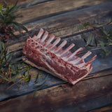 Raw lamb rack on a wooden surface with greenery