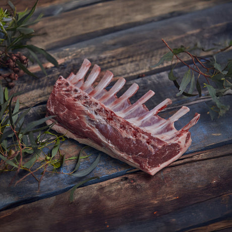 Raw lamb rack on a wooden surface with greenery