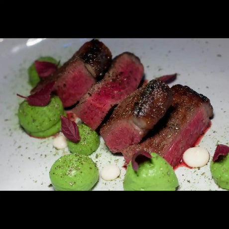Sliced medium-rare beef steak with green pea puree, herbs, and sauce on a white plate