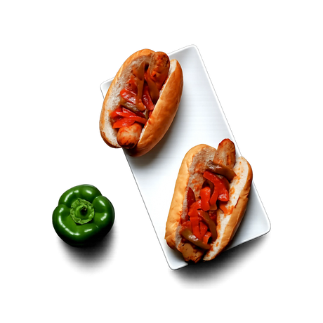 Two hot dogs in white buns topped with red peppers and onions, arranged on a white rectangular plate with a whole green bell pepper on a white background.