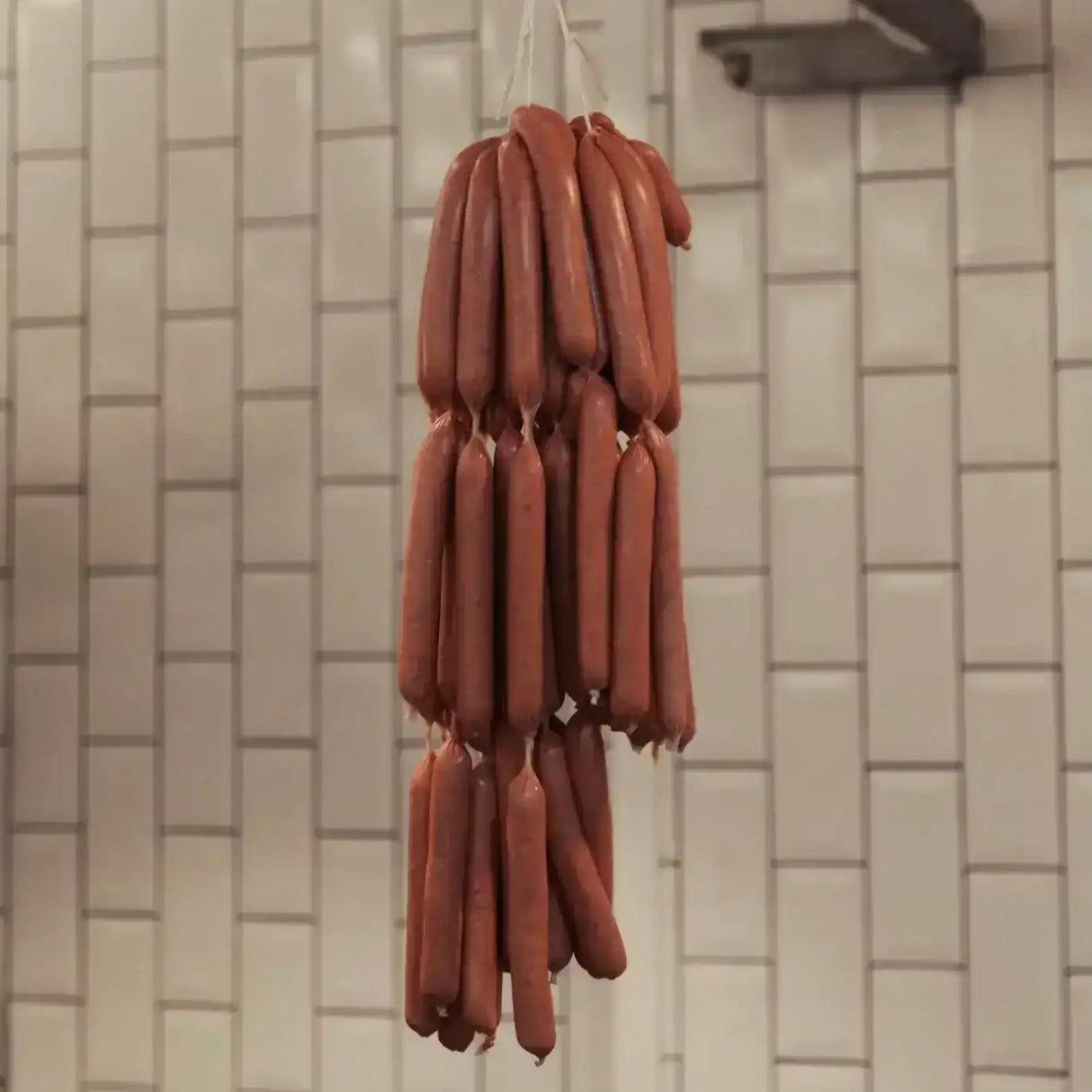 Fresh gourmet sausages hanging in a butcher shop against a white tiled wall