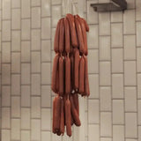 Fresh gourmet sausages hanging in a butcher shop against a white tiled wall