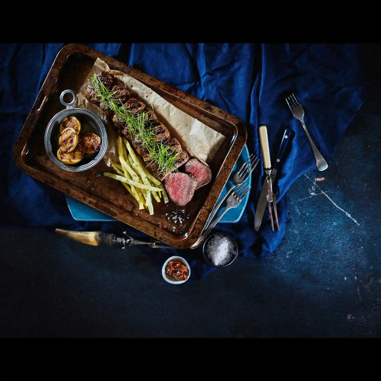 Sliced cooked Australian beef steak with roasted potatoes, beans, and herbs on a tray