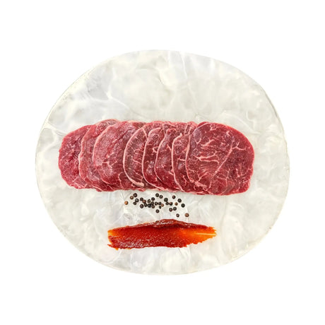 Sliced Wagyu beef with marbling, black peppercorns, and red sauce on white plate