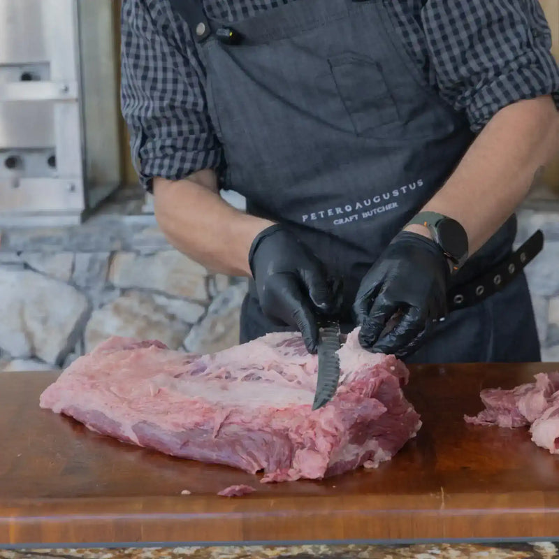 Butcher cutting raw meat on a wooden block with a stone wall background