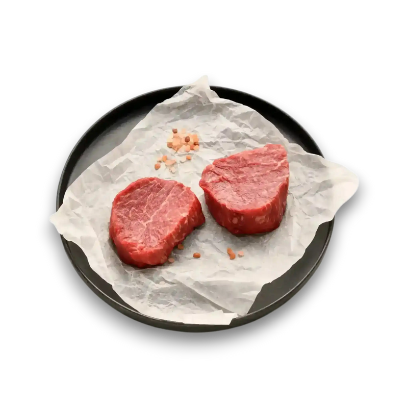 Two raw beef steaks on parchment paper with pink salt, fresh grass-fed beef cuts ready to cook