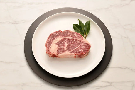 Raw Wagyu rib fillet steak with rich marbling on a white plate, garnished with bay leaves