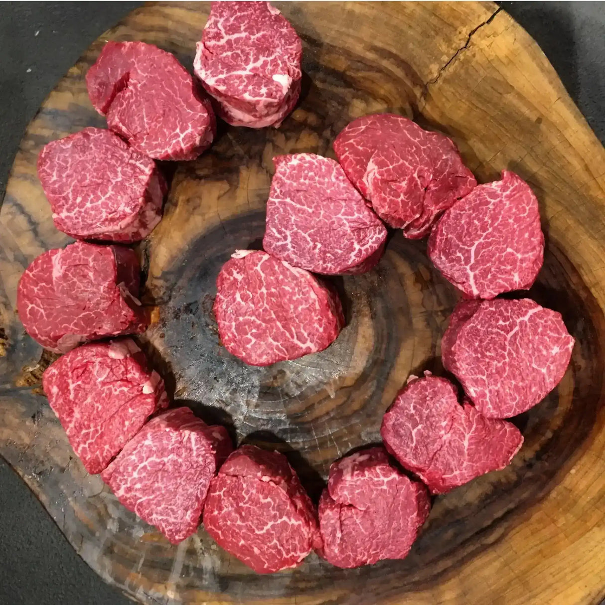 Raw Wagyu beef tenderloin steaks with rich marbling arranged on a rustic wooden board.