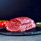Marbled raw beef tenderloin chateaubriand cut on slate platter with tomatoes and oil in background