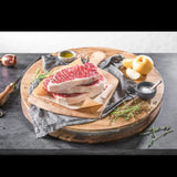Raw Wagyu striploin steak with heavy marbling on a wooden board, surrounded by salt, herbs, and oil.