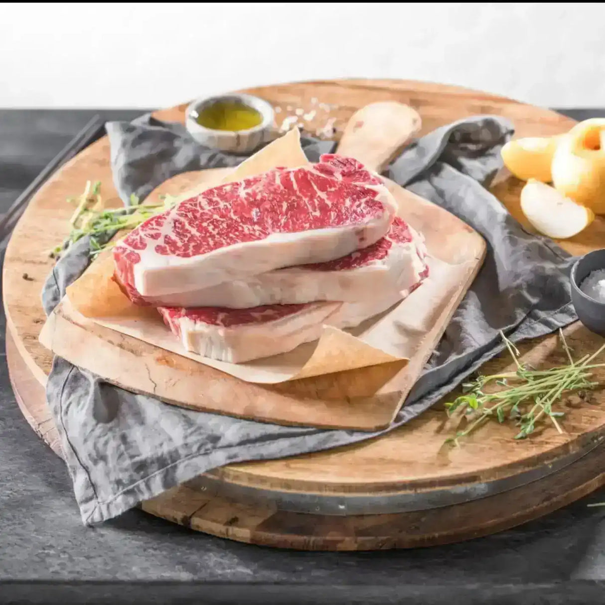 Raw Wagyu striploin steaks with marbling on parchment, on a wooden board with herbs and salt