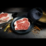 Raw Wagyu striploin steaks with marbled beef on a plate, spices and utensils on dark background