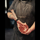 Butcher holding marbled Australian tomahawk steak with apron, raw beef cut on display