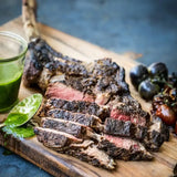 Sliced cooked Wagyu Tomahawk steak on wooden board with green sauce and roasted vegetables