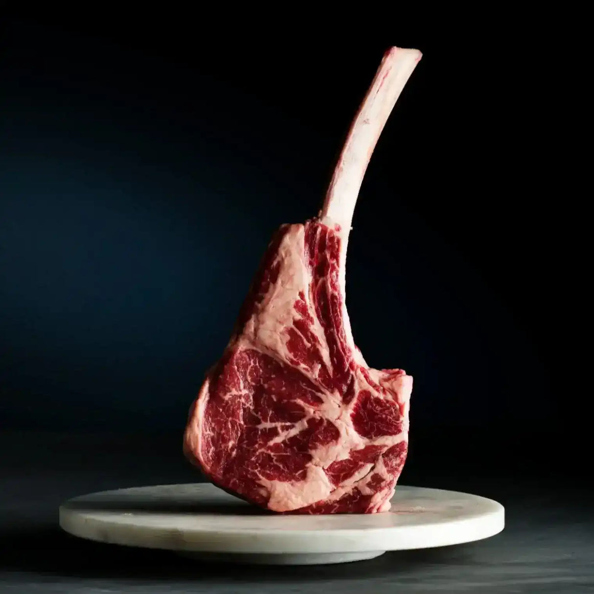 Raw Wagyu Tomahawk steak with marbling standing on a round marble plate