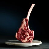 Raw Wagyu Tomahawk steak with marbling standing on a round marble plate